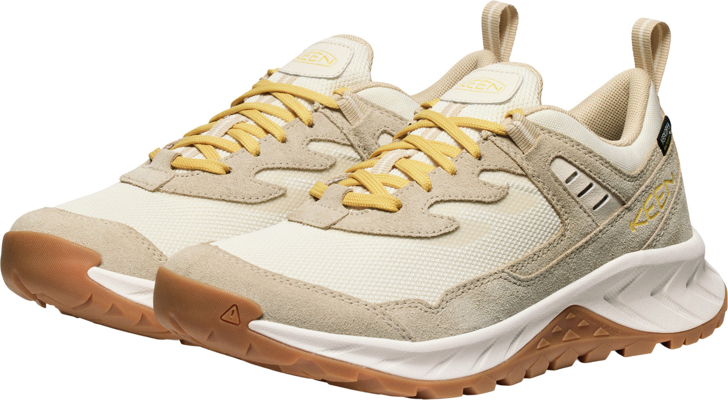 A pair of low-cut athletic shoes with yellow laces and cream-colored suede and fabric uppers. They have tan rubber soles with brown triangle-shaped treads.