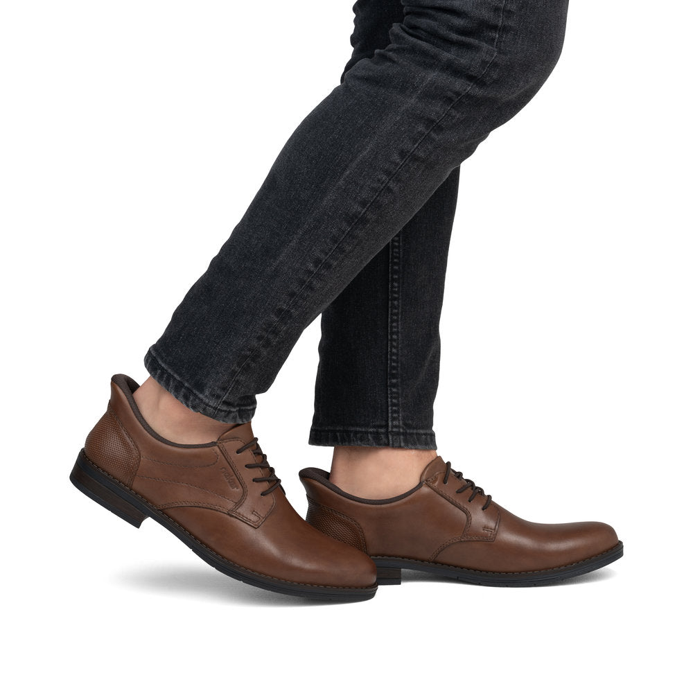 A person wearing brown leather dress shoes and dark gray denim pants, standing.