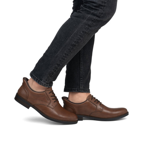 A person wearing brown leather dress shoes and dark gray denim pants, standing.