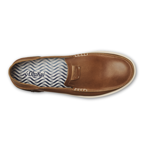 A brown leather slip-on shoe with a cream-colored sole and a wave-patterned insole featuring the brand name OluKai.