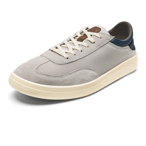 A low-top, lace-up sneaker in light grey suede and mesh, featuring a creamy off-white rubber sole and a dark navy blue accent at the heel.
