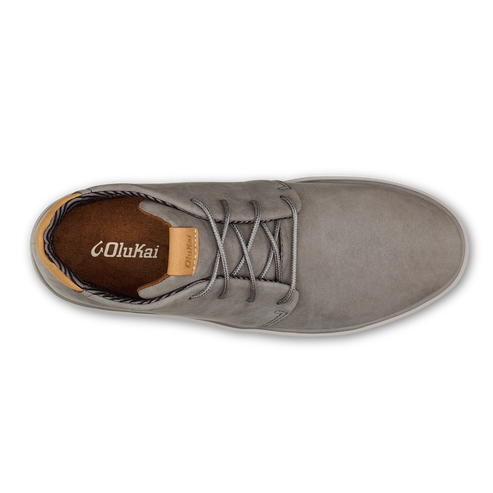 A top-down view of a light gray leather casual shoe with laces, featuring a brown interior lining with the OluKai logo printed on the heel and a small tan tag on the tongue.