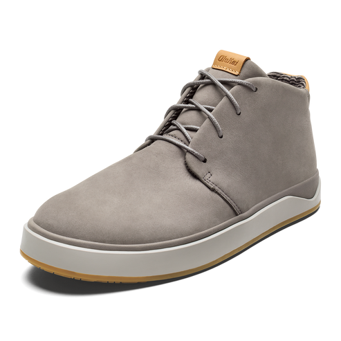 A gray leather chukka-style sneaker with a white midsole, brown gum outsole, and light brown label on the tongue with the text OluKai.