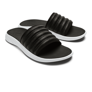 Two black slide sandals with ribbed straps and white soles.