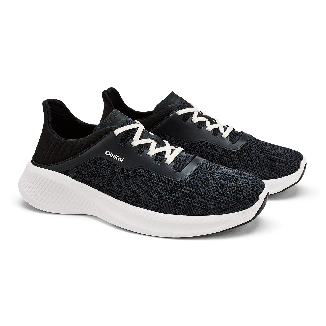 A pair of black athletic sneakers with white laces, a thick white midsole, and the brand name OluKai printed on the side.