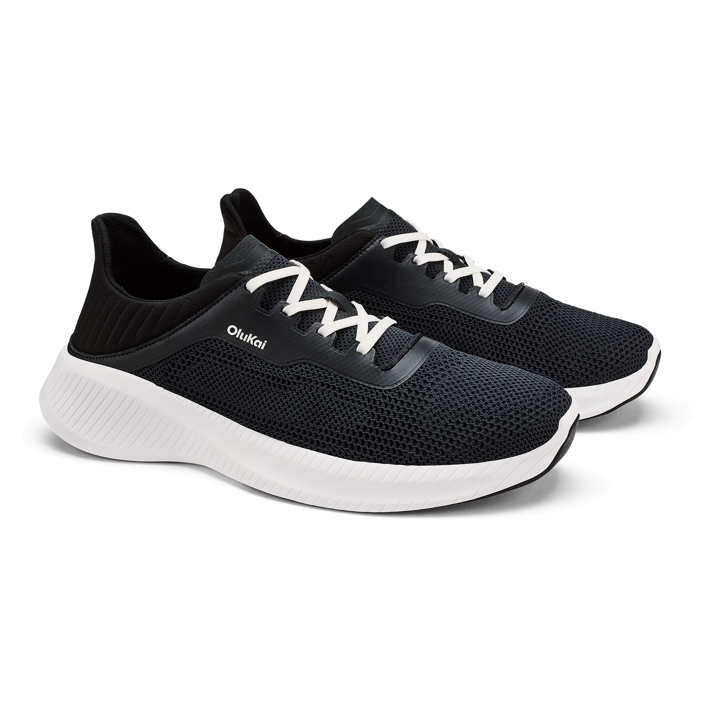A pair of black athletic sneakers with white laces, a thick white midsole, and the brand name OluKai printed on the side.