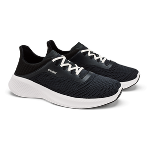 A pair of black athletic sneakers with white laces, a thick white midsole, and the brand name OluKai printed on the side.