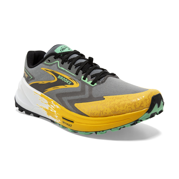 A running shoe with a gray upper, yellow accents at the toe and midsole, black laces, and a white and splatter-painted heel.