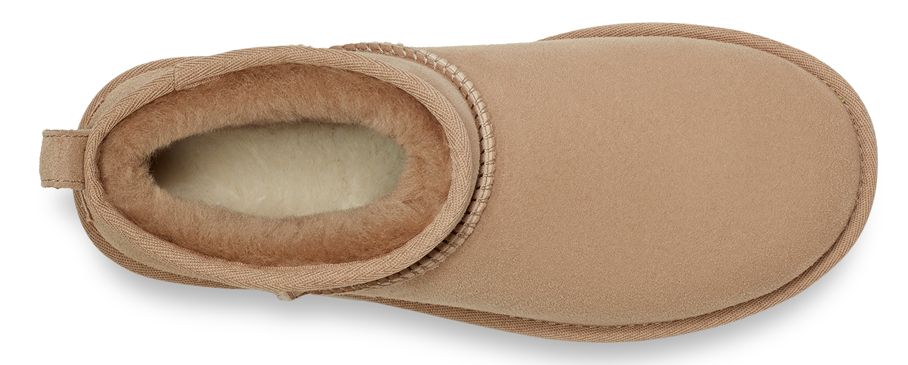 An eye-level, close-up shot of a short, tan-colored boot lined with shearling. The inside and opening of the boot are lined with tan shearling.