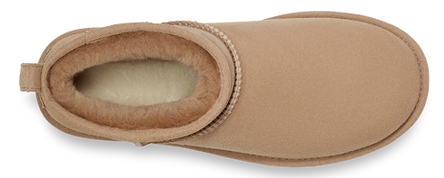 An eye-level, close-up shot of a short, tan-colored boot lined with shearling. The inside and opening of the boot are lined with tan shearling.