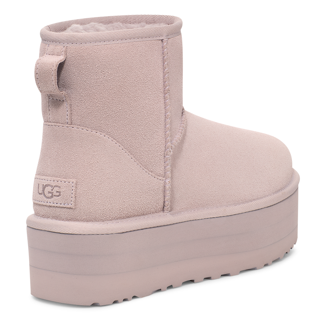 Pale pink suede UGG mini boot with a thick, matching sole and a fabric pull tab on the heel.