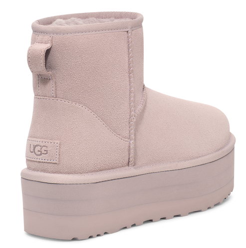 Pale pink suede UGG mini boot with a thick, matching sole and a fabric pull tab on the heel.