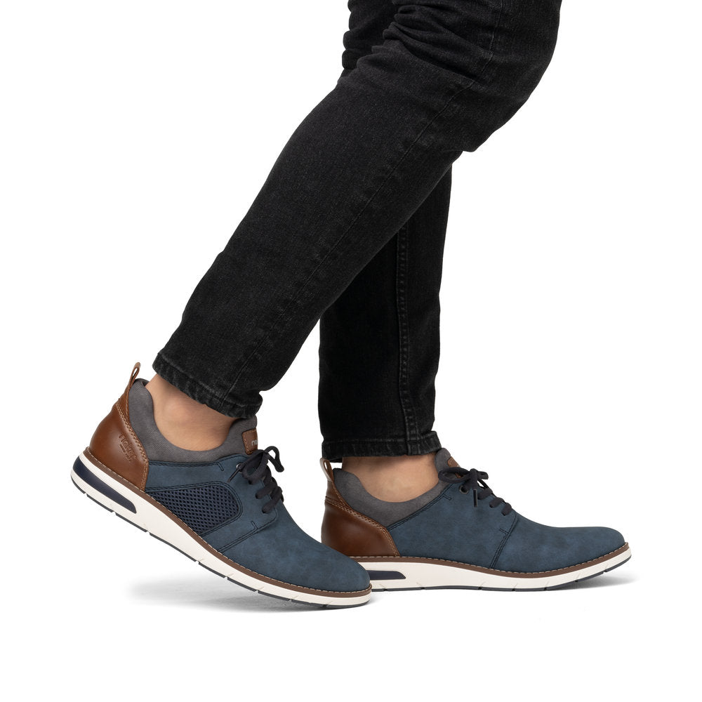 A person is wearing dark blue leather sneakers with a brown heel area and a white sole and black pants.