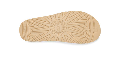 Close-up of the sole of a beige-colored shoe, featuring an intricate tread pattern with the text "UGG" embossed in the center.