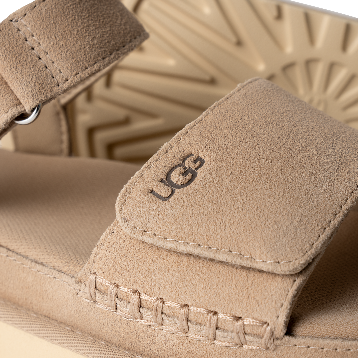 Closeup of light brown sandal with 'UGG' printed on the velcro strap.