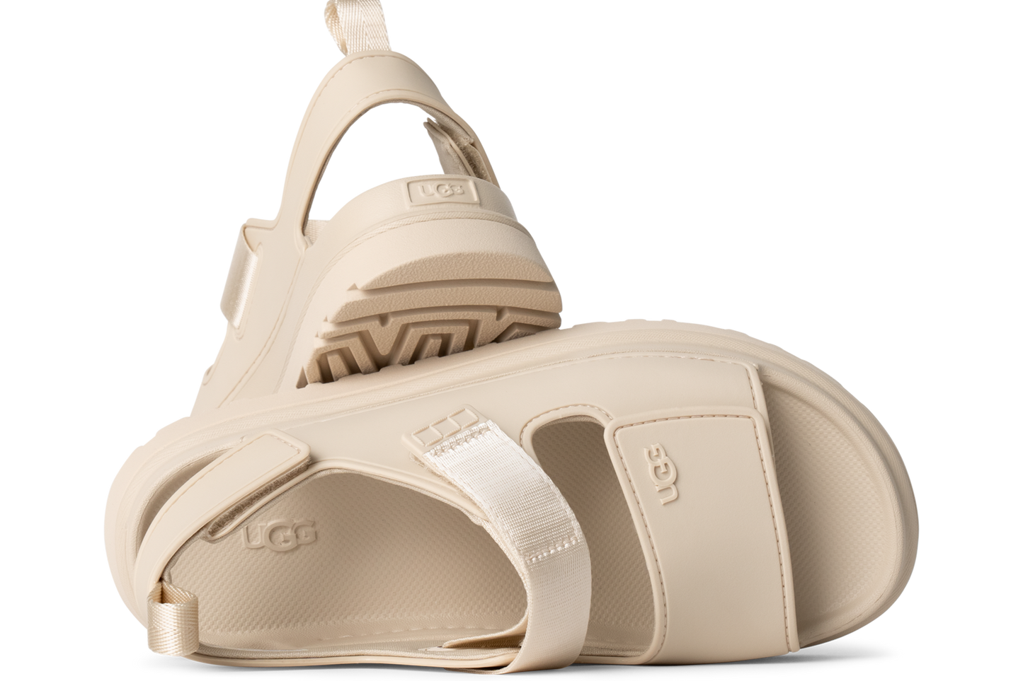 Pair of off-white UGG sandals, one on its side with the sole visible.