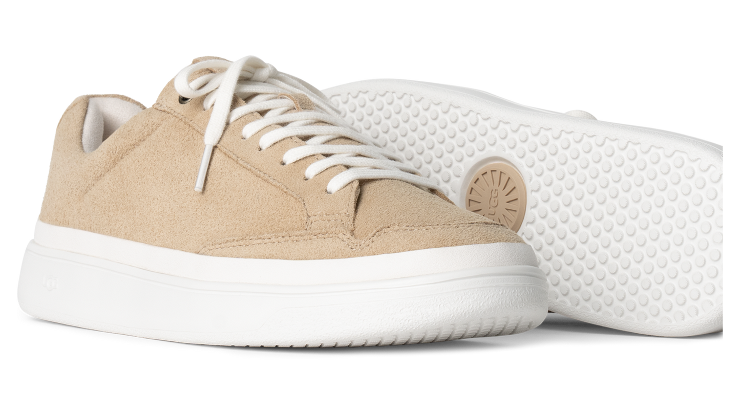 Two low-top sneakers with beige textured uppers, white laces and platform soles, one turned to show the sole with the UGG logo.