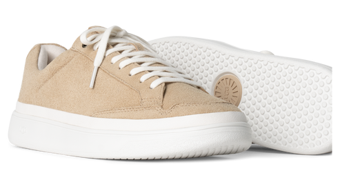 Two low-top sneakers with beige textured uppers, white laces and platform soles, one turned to show the sole with the UGG logo.