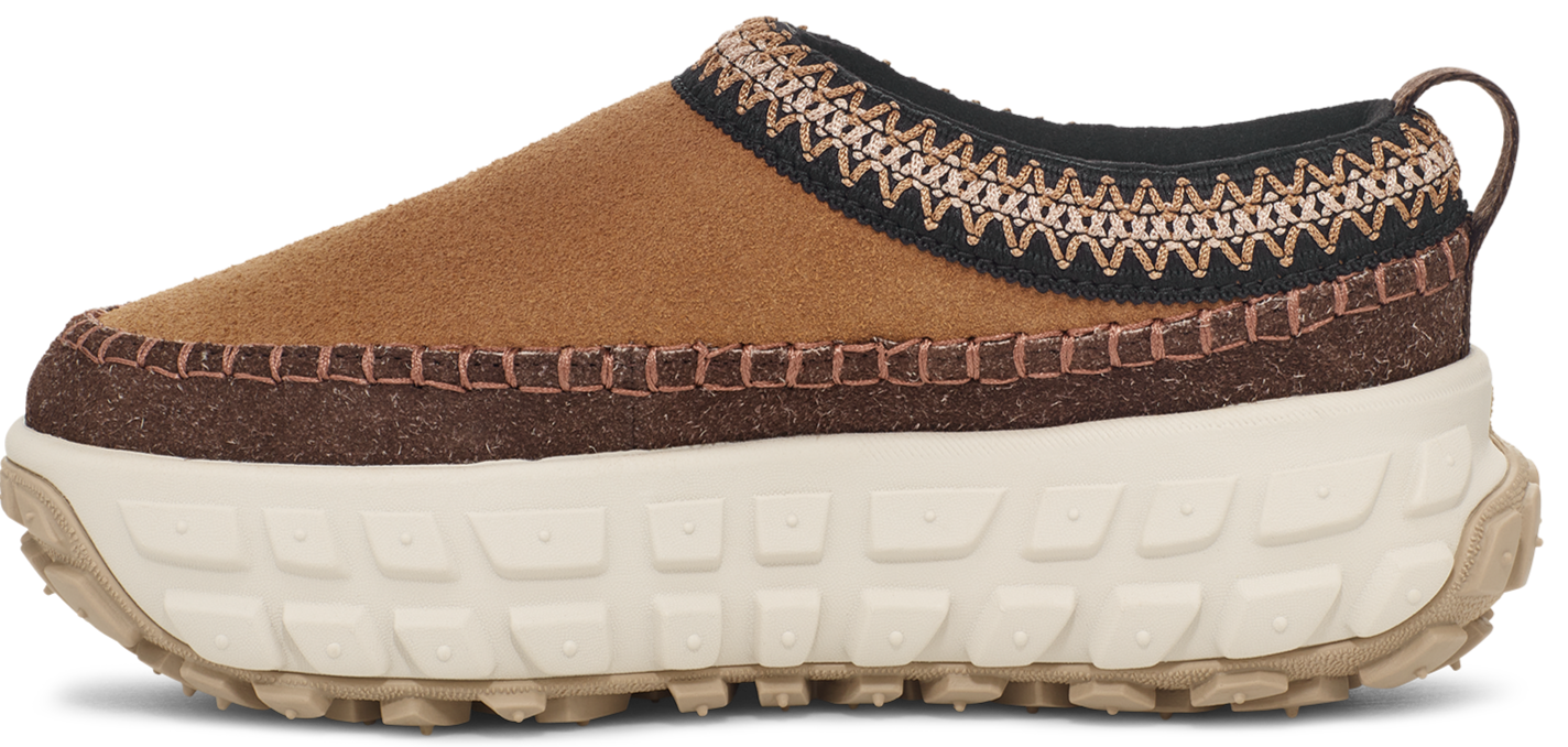 A slip-on shoe with a brown suede upper, decorative stitching, and a thick, off-white sole.