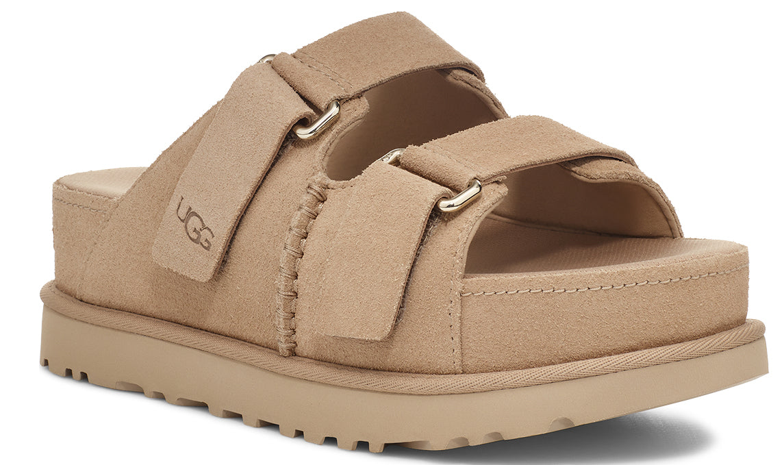 A tan-colored platform sandal with two adjustable straps and the letters 'UGG' on the left strap.