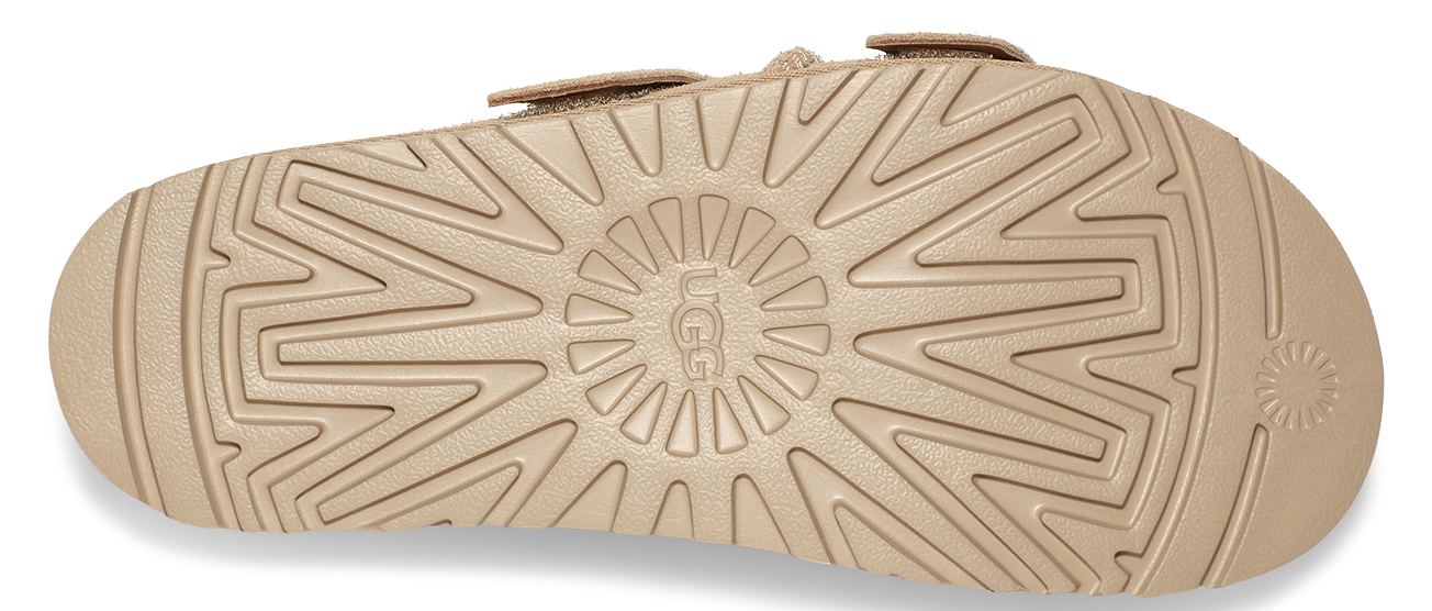The bottom of a tan sandal featuring a circular tread pattern with the word "UGG" visible in the center.