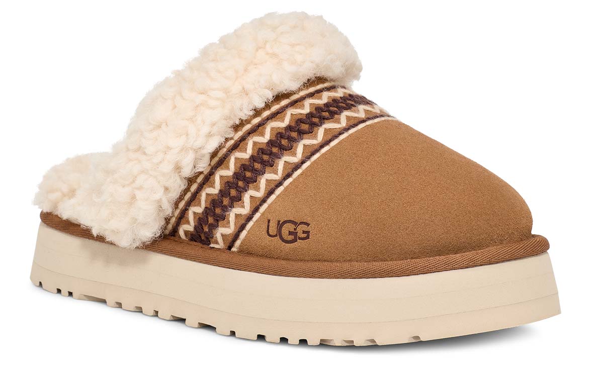 Suede slip-on slipper with faux fur trim, decorative band, and a thick platform sole, showing an UGG logo.