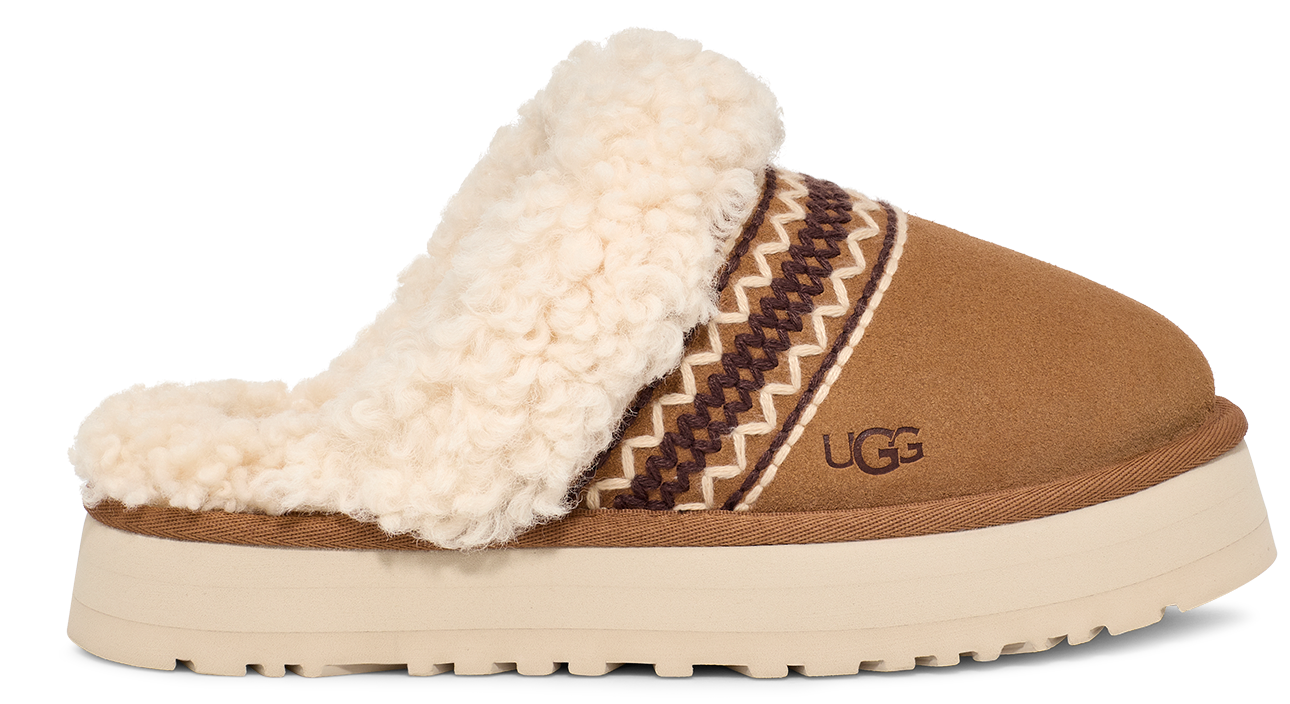 Tan suede slipper with cream-colored sheepskin trim and thick platform sole; a native-inspired design and the letters 'UGG' decorate the side.