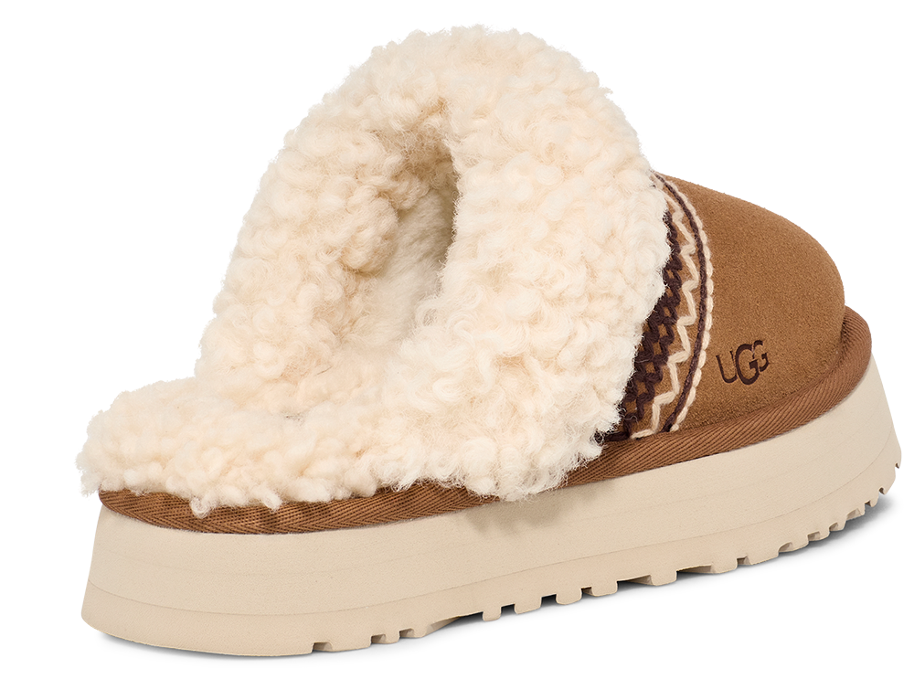 Tan suede platform slipper with cream-colored shearling lining and brown and cream patterned trim, featuring the letters 'UGG' on the side.