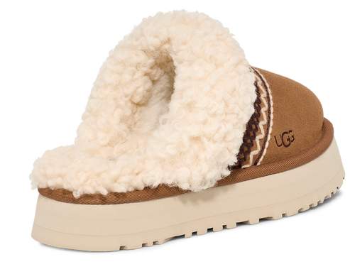 Tan suede platform slipper with cream-colored shearling lining and brown and cream patterned trim, featuring the letters 'UGG' on the side.