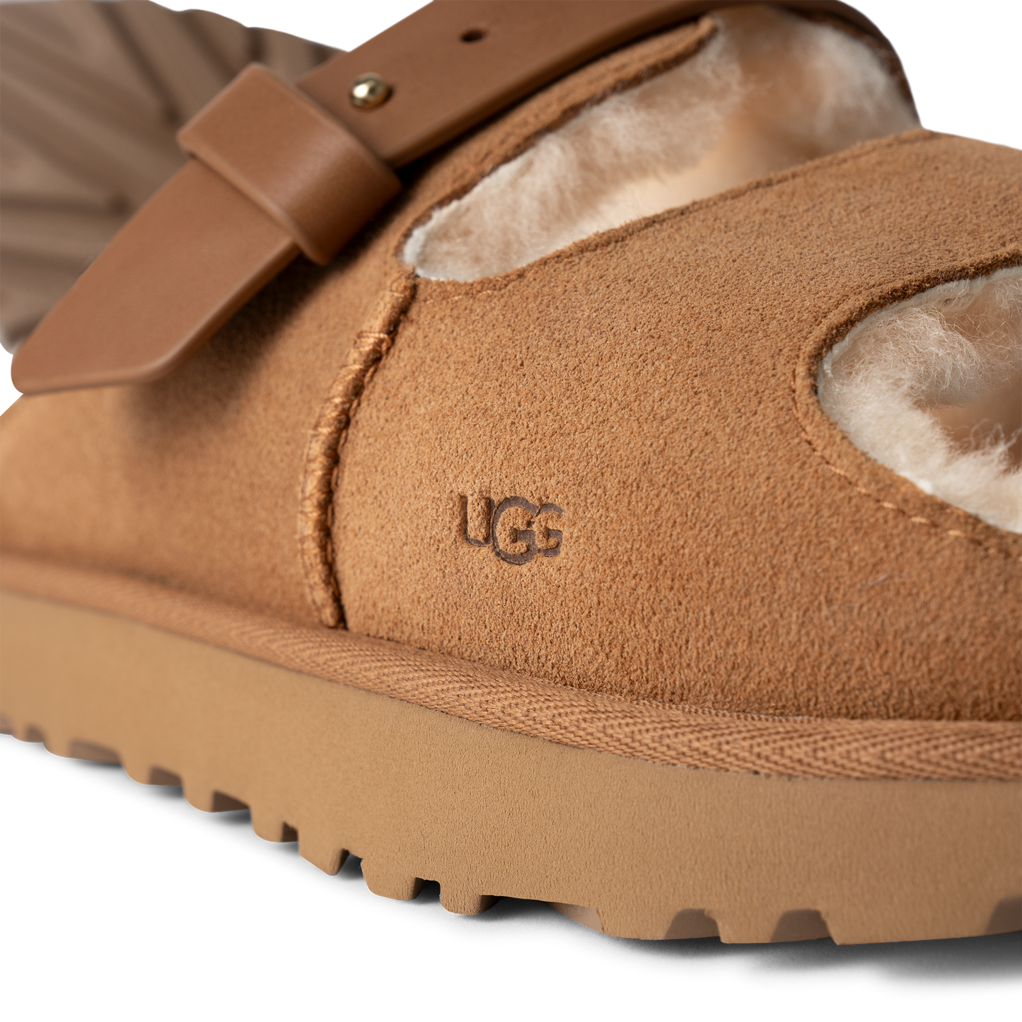 A close-up of a camel-colored suede sandal with shearling lining and an adjustable buckled strap, featuring 'UGG' logo.