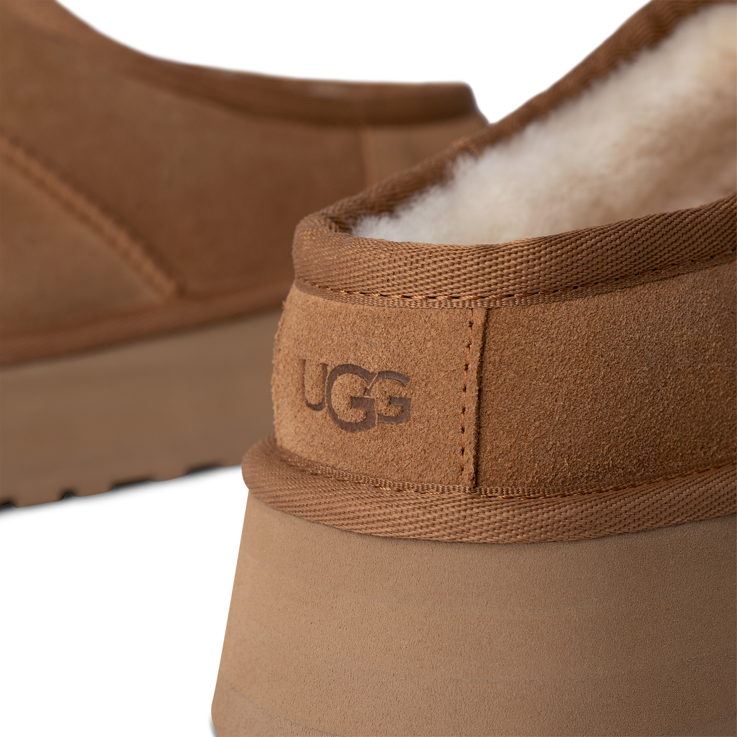 Close-up of tan slipper with visible UGG logo, and off-white interior.