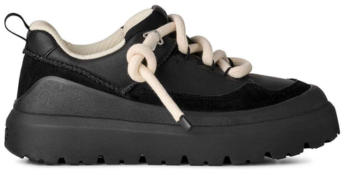 A black sneaker with a thick, rugged platform sole, featuring cream-colored rope laces, a black suede and synthetic leather upper, and a cream-colored lining at the heel collar.