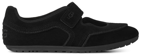 A black suede Mary Jane-style shoe with a hook-and-loop strap across the instep, featuring the embossed letters UGG on the strap and on the heel, set on a flat, ridged rubber sole.