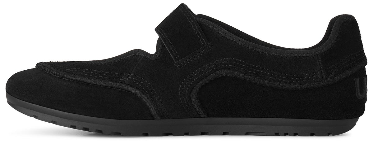 A black suede minimalist sneaker with a single Velcro strap over the instep and a thin, flat black rubber sole.