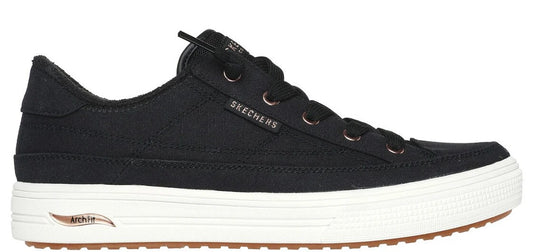 A black sneaker with white sole and brown tread, featuring visible “SKECHERS” branding.