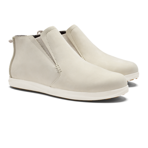 A pair of slip-on, off-white ankle boots with elastic side panels, a rounded toe, and a flat white sole.