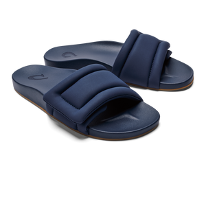 A pair of navy blue, wide-strap slides with a padded, rectangular design and a small embossed logo on the footbed.