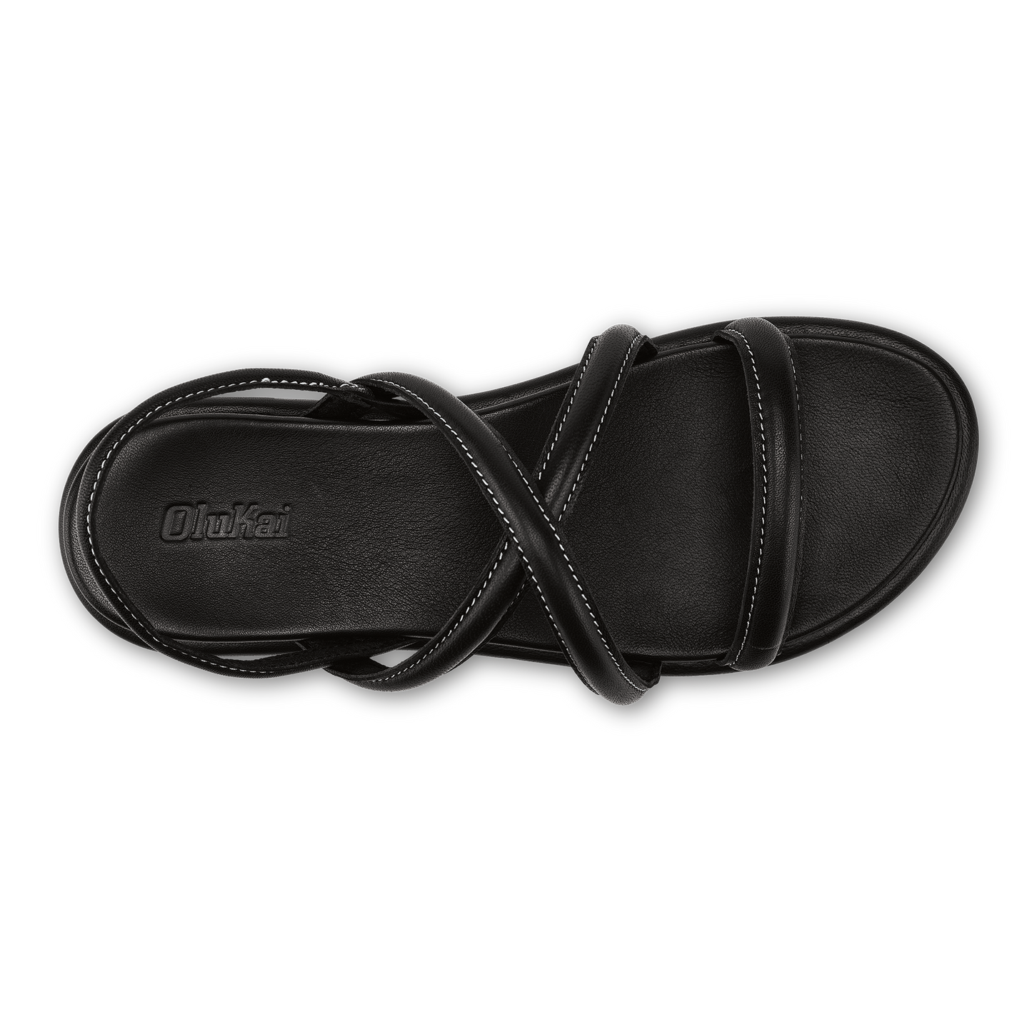A top-down view of a black women's flat sandal with a cushioned footbed, featuring crisscrossing thin straps across the instep and an ankle strap with visible stitching and the embossed brand name OluKai on the heel.
