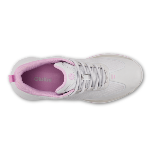 A top-down view of a white athletic sneaker with pink interior lining and the text 'OluKai' printed on the insole.