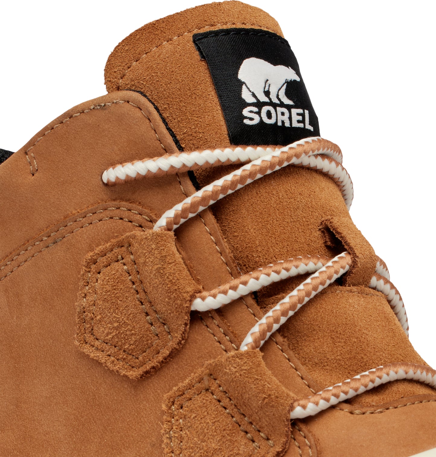 Tan suede shoe close-up with a black patch bearing a polar bear logo and the word 'SOREL', featuring white and brown rope laces.