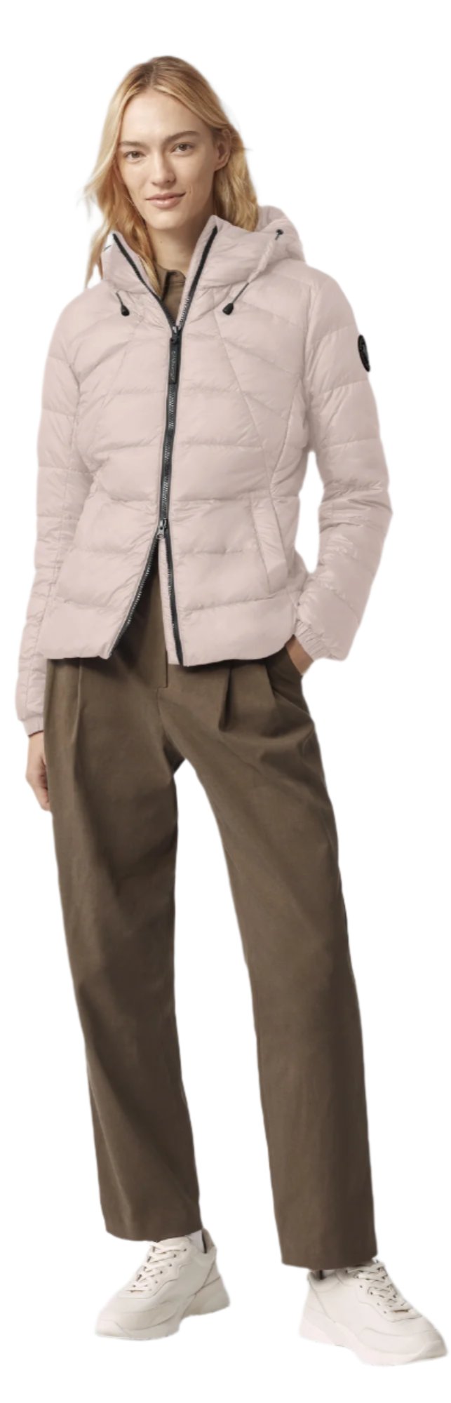 A woman is wearing a pink puffer jacket and green pants with white shoes.