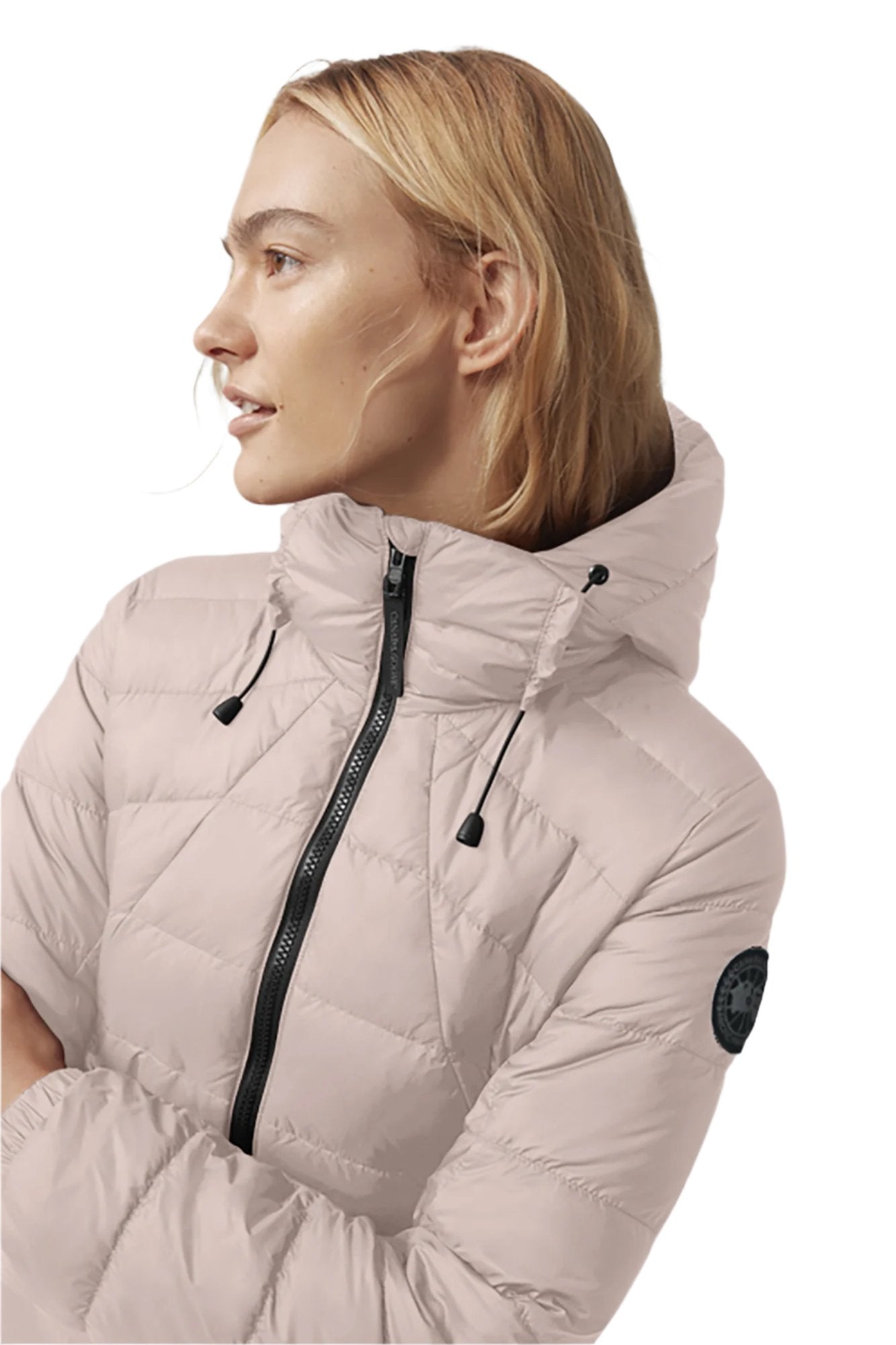 Person wearing light pink quilted down jacket with hood and black zipper, facing left.