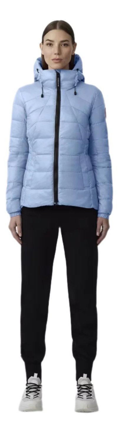 A woman stands wearing a light blue hooded puffer jacket, black pants, and white sneakers.