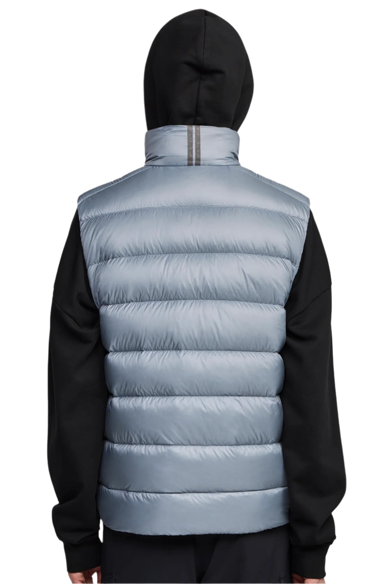 Back view of a person wearing a light blue puffer vest with horizontal quilting and a black hooded sweater.