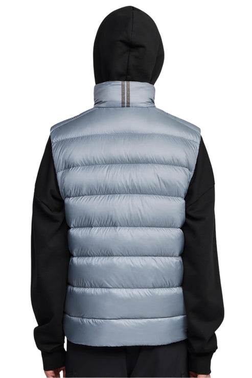 Back view of a person wearing a light blue puffer vest with horizontal quilting and a black hooded sweater.