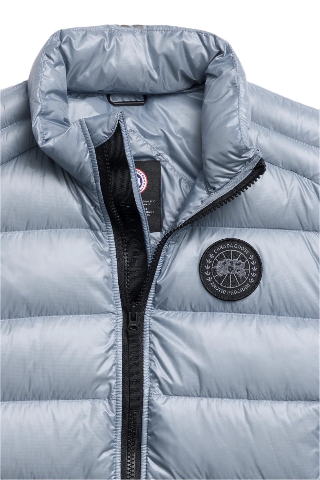 Close-up of a light blue quilted down vest with a black zipper and a circular logo on the chest.