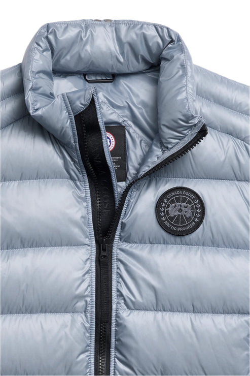 Close-up of a light blue quilted down vest with a black zipper and a circular logo on the chest.