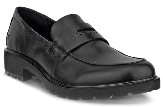 A black leather penny loafer shoe featuring a thick lug sole, rounded toe, and a classic strap across the vamp with decorative perforations.