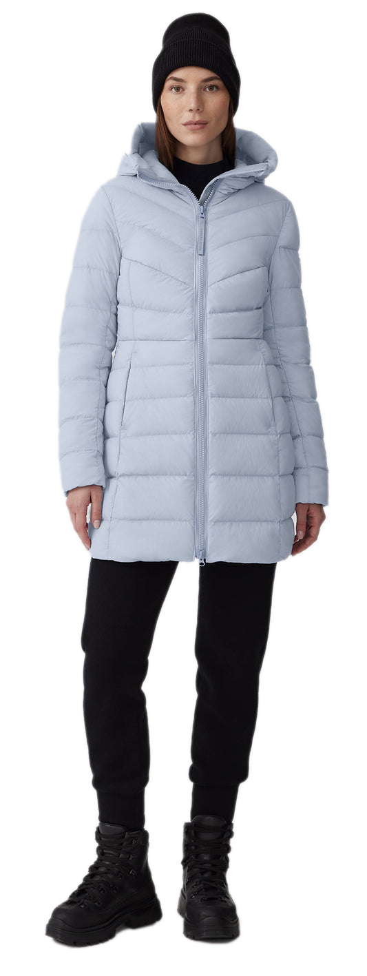 A woman wearing a black beanie, a light blue puffer jacket, black pants, and black boots.