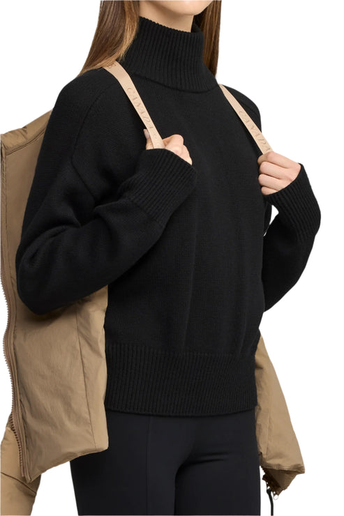 Woman wearing a black turtleneck with a beige jacket draped around her shoulders.